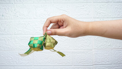 Hand holding ketupat replica or rice dumpling over white wall