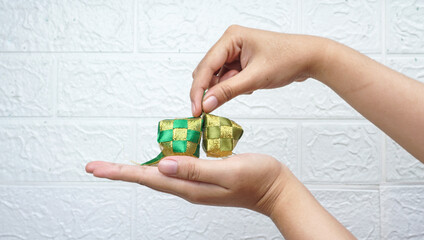Hand holding ketupat replica or rice dumpling over white wall