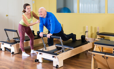 Fototapeta na wymiar Elderly man doing exercise with her personal trainer in pilates studio