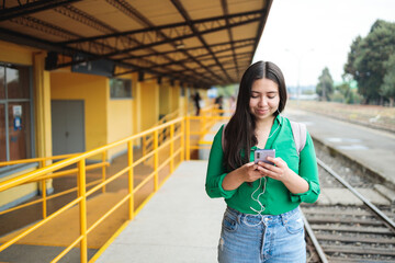 Young hispanic girl chatting and browsing social media on her phone, in a train station. Copy space