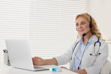 Doctor with laptop and headphones consulting patient in clinic. Online medicine concept