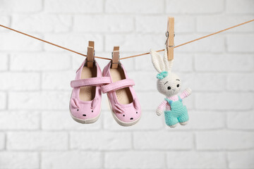 Cute pink baby shoes and crochet toy drying on washing line against white brick wall