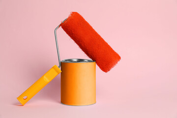 Can of orange paint and roller on pink background
