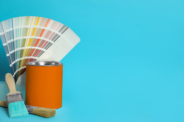 Can of orange paint, color palette samples and brushes on turquoise background. Space for text