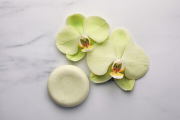 Fototapeta na wymiar Solid shampoo bar and orchid flowers on white marble table, flat lay. Spa composition