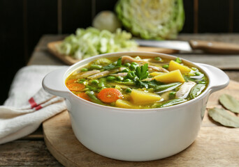 Saucepan of delicious vegetable soup with chicken on wooden table