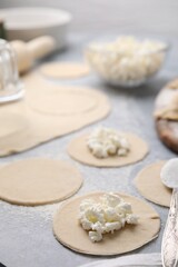 Fototapeta na wymiar Process of making dumplings (varenyky) with cottage cheese. Raw dough and ingredients on grey table, closeup
