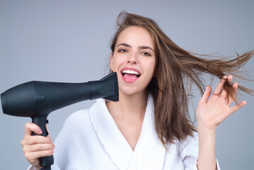 Beautiful woman drying her hair with a hairdryer isolated on studio background. Young woman with blow dryer drying hair, making hairdo. Closeup portrait of girl in drying hairstyle.