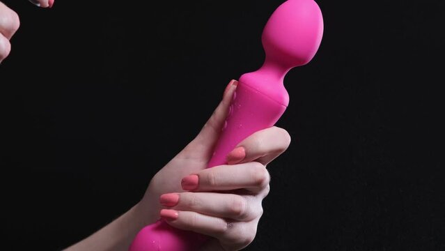 Girl holds in her hands a pink massager for sex on a black isolated background. Sprays with antiseptic, wipes with hand. Vibrator for masturbation. For sex shop
