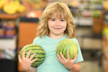 Fototapeta premium Portrait of child with watermelon in a food store. Supermarket shopping and grocery shop concept. Shopping kids. Child buying grocery in supermarket. hold shopping basket.