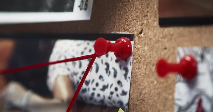 Detail on red pin. Detective's hand wraps the red string around the pin and connects the pieces of the case.