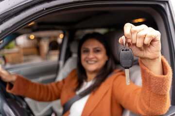 Smiling Indian woman driving new car, holding keys, selective focus. Transportation, car sharing...