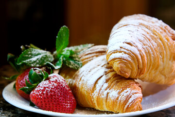 Powdered sugar sprinkling onto a croissant on a white plate a croissant with strawberries two ripe strawberries are sprinkled with powdered sugar mint leaves red transparent sauce flows off it
