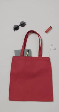 Vertical video of red bag with sunglasses, notebook and lipstick, copy space, slow motion