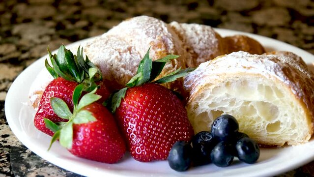 no on plate female hand lays different fresh blueberries or lohina strawberries as well as a fresh soft croissant sprinkled with powdered sugar lunch dessert tasty healthy food