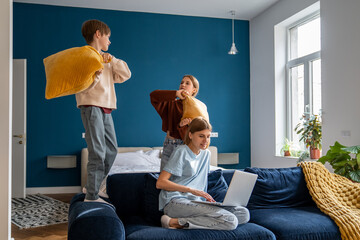 Work-family balance. Mother juggling working from home with looking after children, combining remote work with spending more time with family. Mom using laptop while her kids playing on background