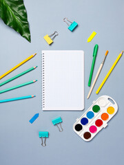 Top view arrangement with notepad with white sheets and pens, pencils, paper clips and other office supplies on blue background