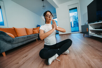 A young woman is practicing yoga and relaxing with headphones on her head in a modern apartment