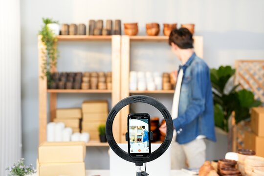 Asian influencer man record live video broadcast by smartphone with ring light for promote vase handmade product at home