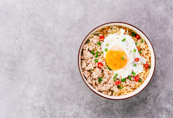 Instant noodles or ramen with minced pork and boiled egg in white bowl on the table with copy space - top view