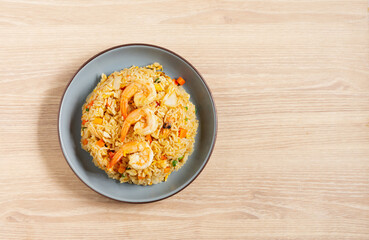 Fried rice with vegetables and sea prawns, carrots, eggs, and tomatoes. Chinese Thai food is served on a blue plate on a wooden table in the kitchen, top view.
