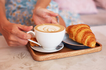 female hands with a cup of coffee and a croissant in a cafe.