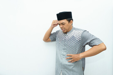 Portrait of an Asian Indonesian Muslim man put his hands on head and stomach for headache gesture during fasting ramadan