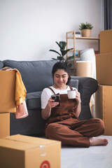 New house, woman chilling using smart phone with the boxes and excited about buying a house with a mortgage loan. Young asian woman first time buyers unpacking in dream home, apartment