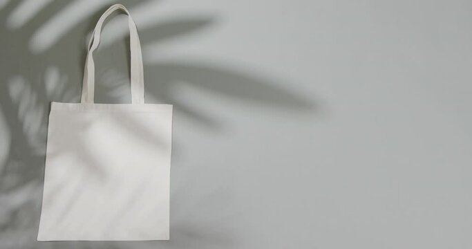 Leaf shadow moving over white bag on grey background, copy space, slow motion