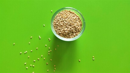 White sesame seeds in a glass bowl with a few extra seeds scattered onto a pretty green background.