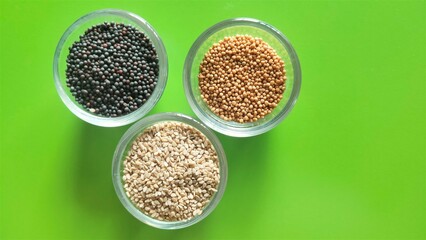 Yellow mustard, black mustard and white sesame seeds in separate bowls against attractive green background