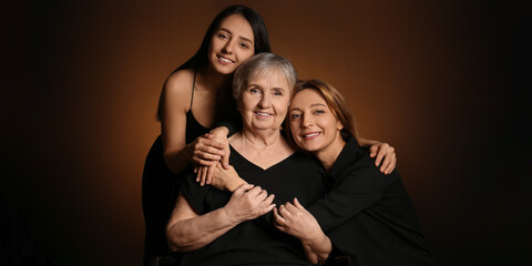 Portrait of beautiful mature woman, her daughter and mother on dark brown background