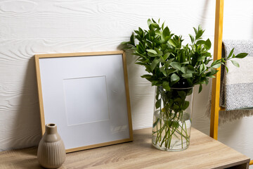 Wood empty frame with copy space, plant in pot on table and towel hanging against white wall