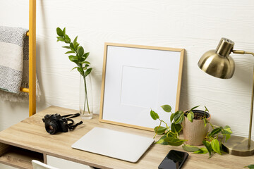 Empty frame with copy space, plants, technology devices on table against white wall