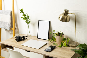 Empty frame with copy space, plants, technology devices on table against white wall