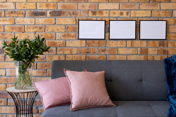 Black empty frames with copy space and plant against brick wall in room with couch