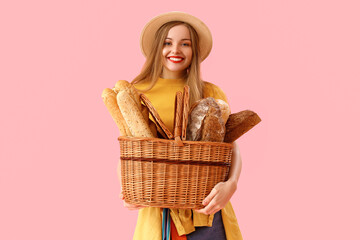 Young woman in hat with basket of fresh bread on pink background