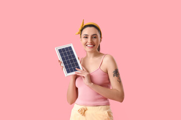 Pretty young woman with portable solar panel on pink background