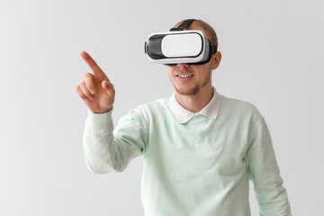 Young man using VR glasses on light background