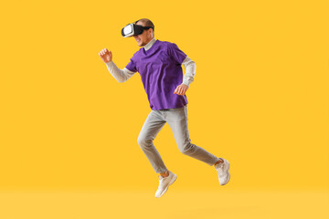 Fototapeta na wymiar Jumping young man with VR glasses on yellow background
