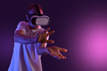 Young man using VR glasses on dark violet background