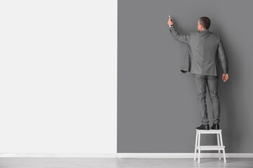 Mature business consultant with marker on stepladder near black and white wall, back view