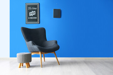 Stylish grey armchair, pouf and poster with text IT'S TIME FOR A CHANGE near blue wall