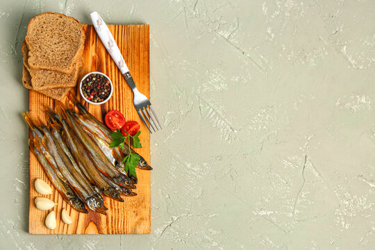 Board with tasty smoked capelin and bread pieces on grey background