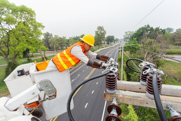 Asian electrician with crane truck is installing cable lines and electrical transmission on electric power pole against blue sky background