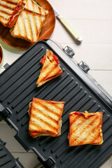 Delicious sandwiches in modern electric grill on white wooden table
