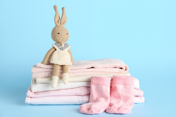 Stack of baby clothes, socks and toy on color background