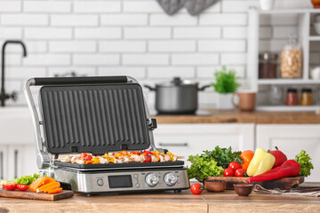 Modern electric grill with tasty chicken skewers and vegetables on table in kitchen