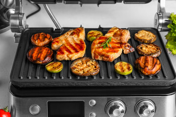 Modern electric grill with tasty steaks and vegetables on light background