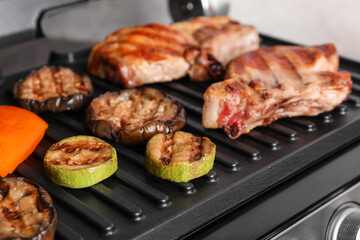 Modern electric grill with tasty steaks and vegetables on light background, closeup